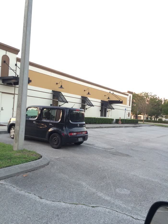 Evening light on the storefront, cream walls under a gold band, awnings uncovered and a car parked in front.