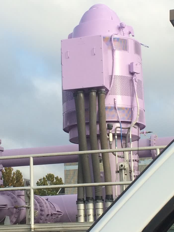Tall industrial machinery and pipes painted pale lilac, thick grey cables running down past a white handrail.
