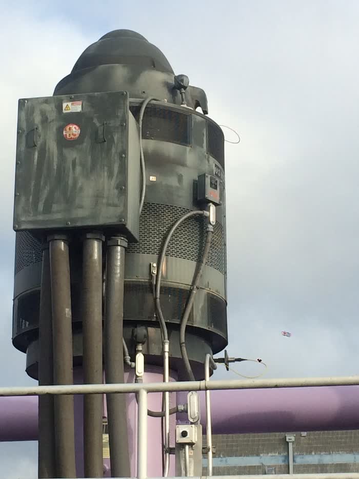 Weathered dark grey machinery streaked with grime, a lilac pipe and white handrail crossing below it.