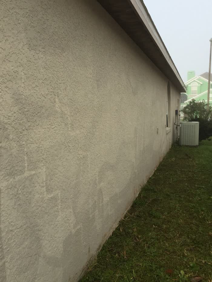 A long side wall seen down its length, pale patched areas across the lower half, grass alongside.