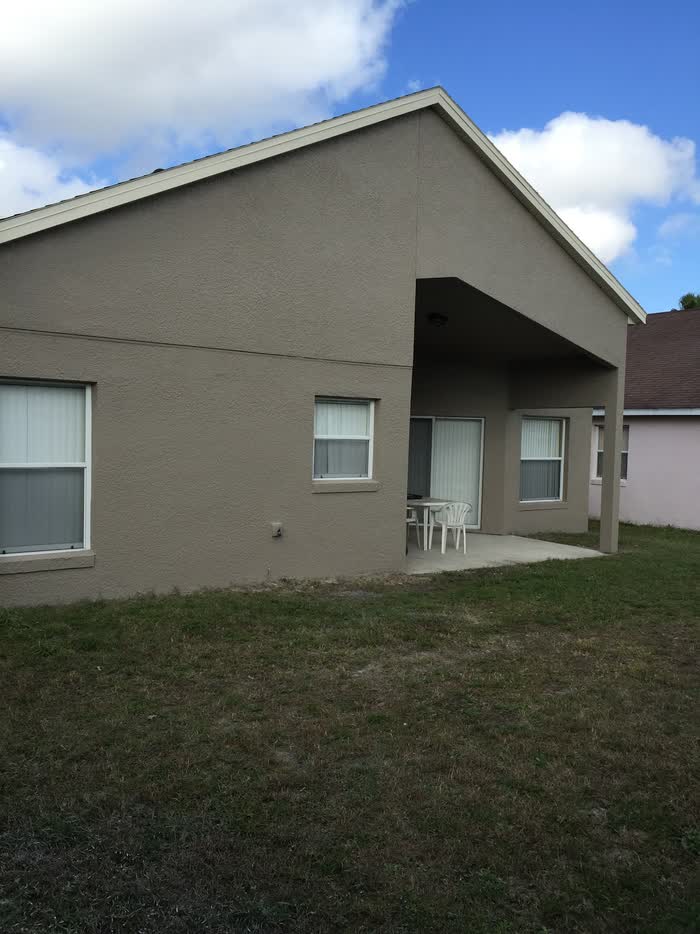 Beige house corner with a covered patio, two plastic chairs and a table on the slab.