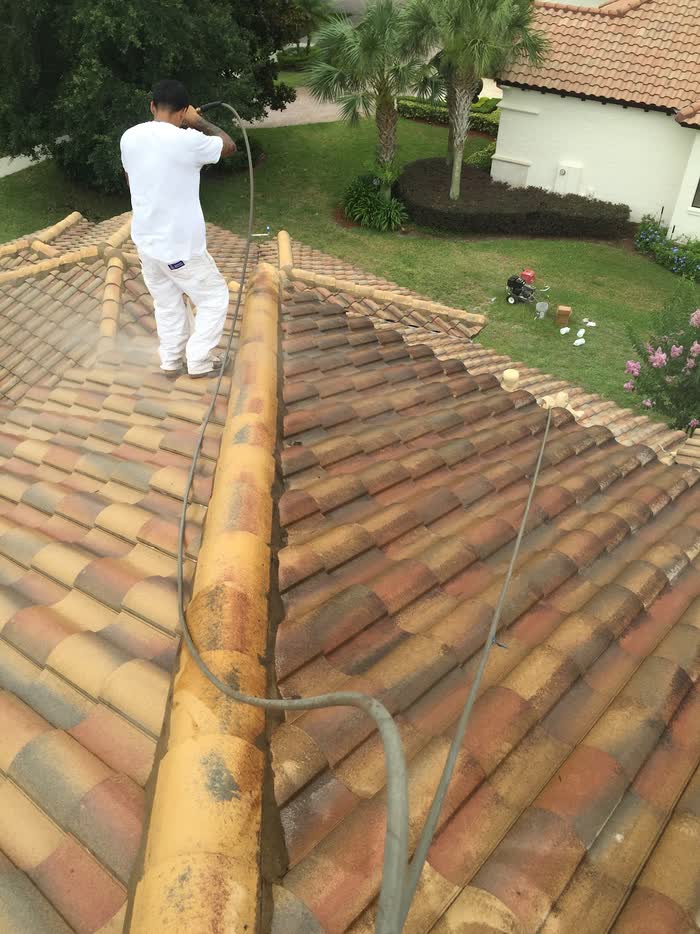 Seen from above, a hose trails behind a worker as one slope of the tiled roof turns pale.