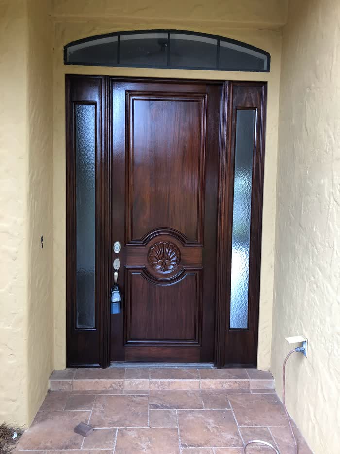 Deep reddish-brown front door with a fresh glossy finish, framed by pale yellow walls and frosted sidelights.