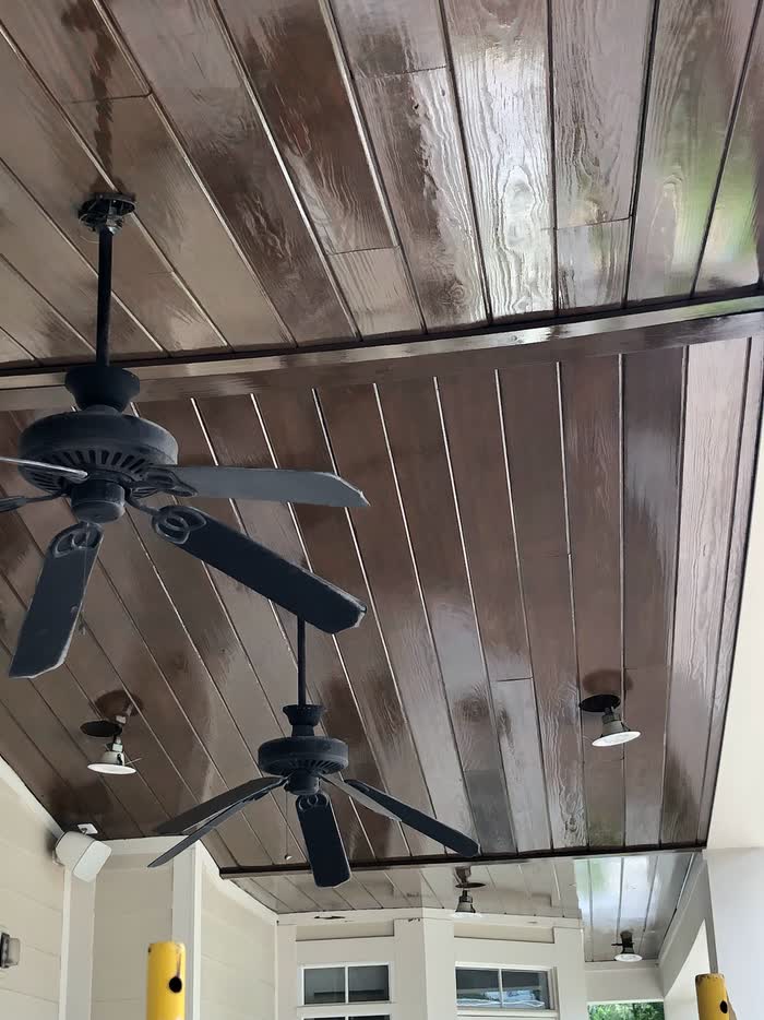 Looking up at a porch ceiling of dark stained boards with two black ceiling fans and small lights.