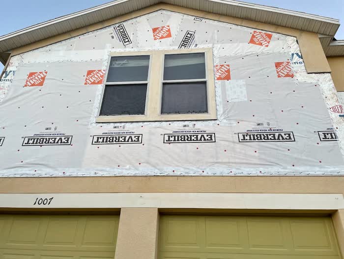 White weather wrap now covers the gable, taped around the window and dotted with red-capped fasteners.