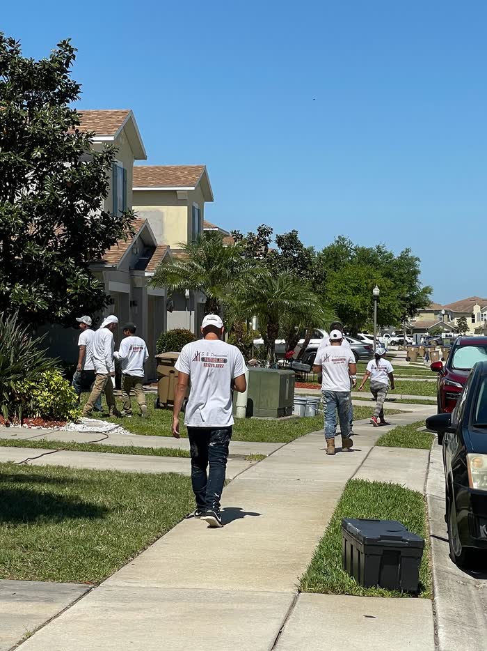 Several of the crew in matching white shirts walking up a residential sidewalk under a clear blue sky.