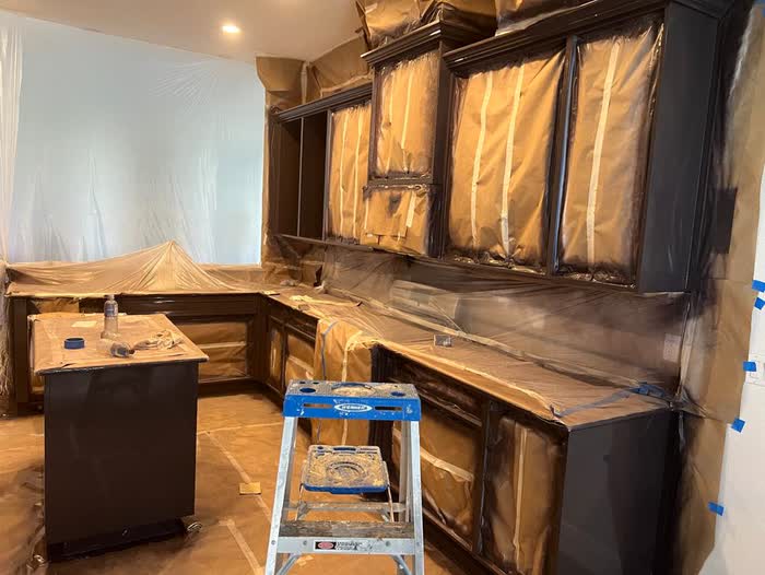 Near-black cabinets wrapped in paper and plastic, a step ladder standing open in the middle of the room.