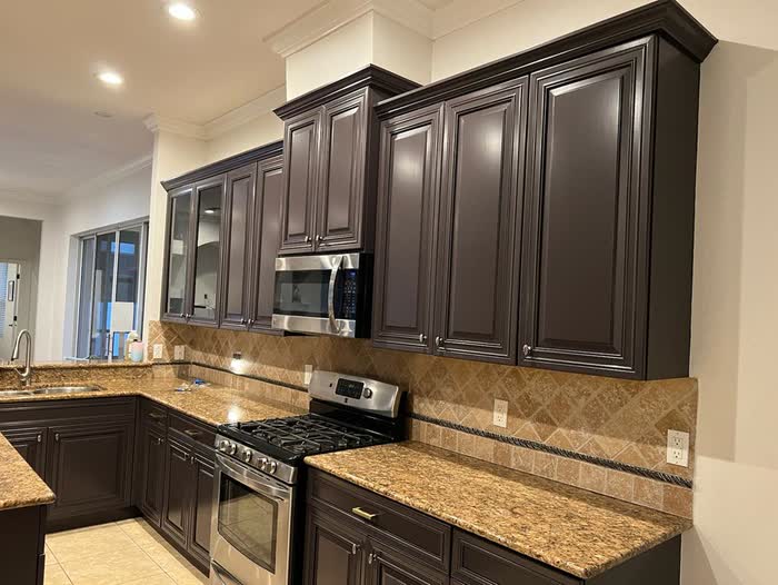 Finished dark brown kitchen cabinets under white crown moulding, with a stainless microwave above the range.