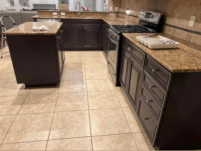 Wide view across a kitchen: dark brown cabinets, flecked brown countertops and pale square floor tiles.