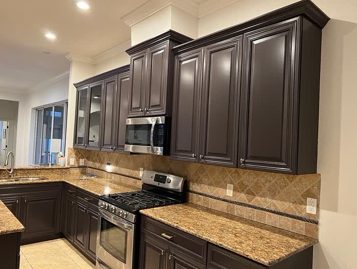 Corner of a kitchen with dark cabinets, one glass-front door, and tan square tiles behind the range.