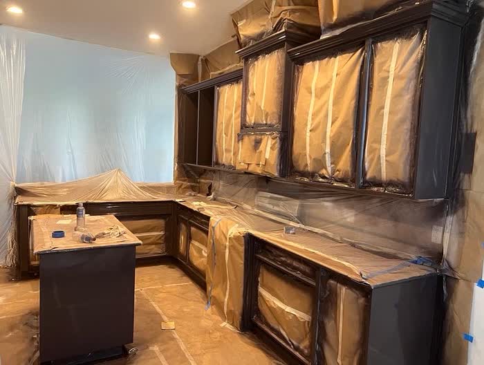 Cabinets and a small island covered in paper and plastic, sheeting taped over the wall in the corner.