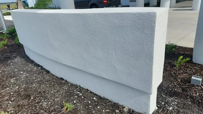 Freshly coated white wall curving along a mulch bed, with a building and driveway behind.