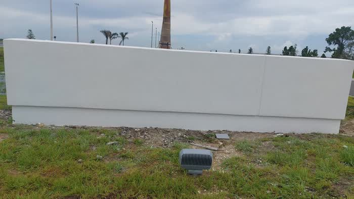 White wall standing on bare ground under a cloudy sky, a light fixture resting on the grass.
