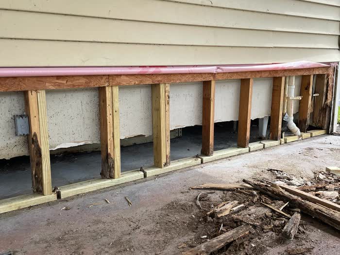 Opened-up base of a wall, horizontal cream boards above and upright posts set into the gap.