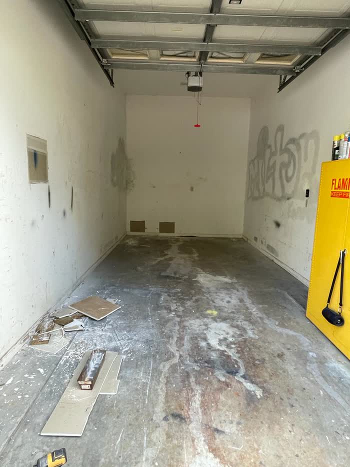 The garage before the work: marked walls with graffiti on one side and a heavily stained concrete floor.