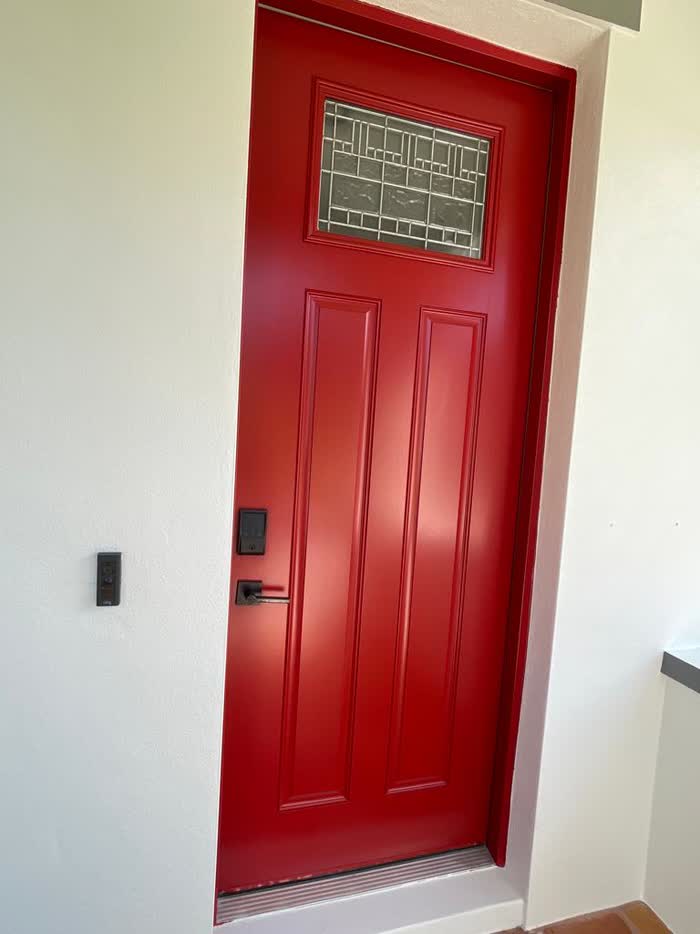 Bright red front door with a leaded glass panel and black handle, set in a pale doorway.