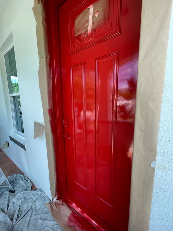 Wet red paint gleaming on a panelled door, its frame masked with paper and the floor sheeted below.