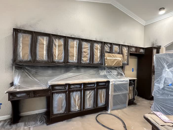 Long run of dark cabinets masked with plastic, spray haze showing on the textured wall above.