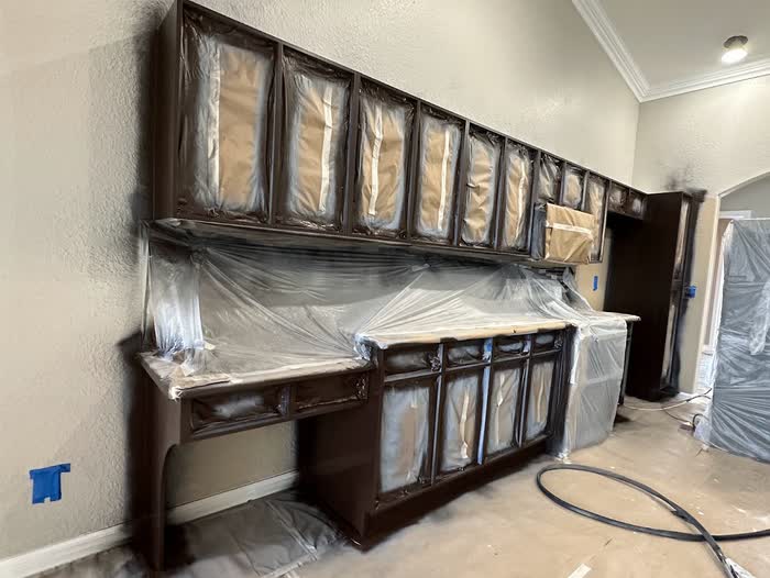 Dark brown cabinets partway through the job, glass doors masked off with plastic sheeting and paper.