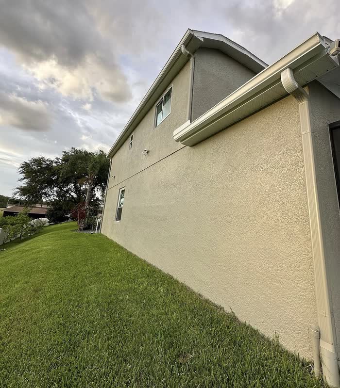 Cream side wall of a two-storey home rising above a green lawn at dusk.