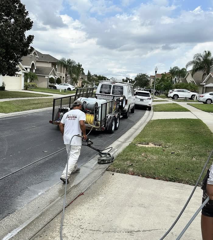 Behind a round surface cleaner, a worker walks a driveway apron, leaving a bright clean strip behind him.