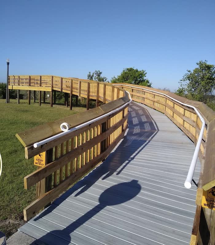 A curving raised walkway with pale bare railings and grey boards under a clear blue sky.