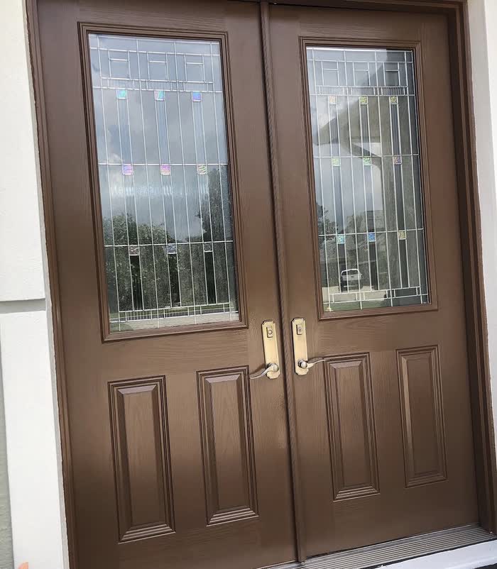 Brown double front doors with tall decorative glass panels and pale handles, masking removed.