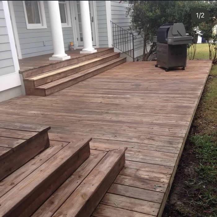 Wide deck of faded grey boards with broad steps and a grill parked by the porch.