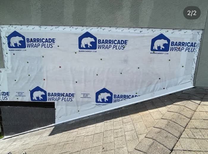 White printed sheeting stapled across a wall opening next to a shingle roof.