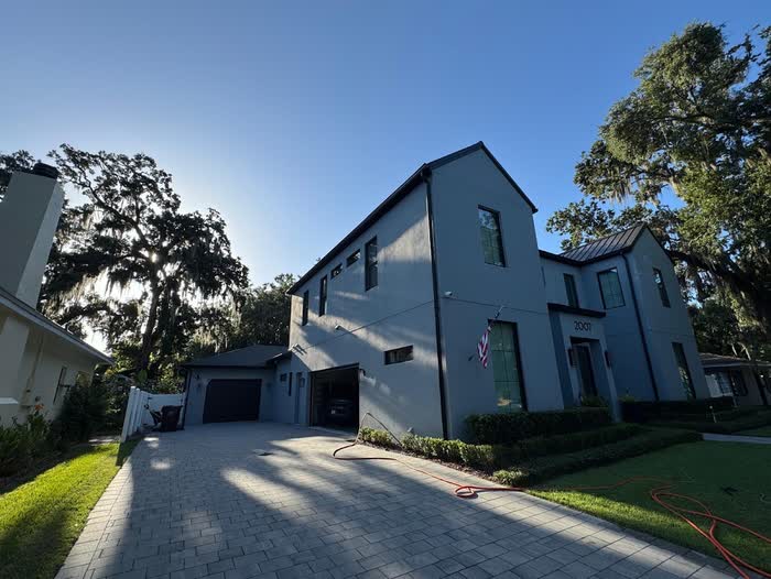 Two-storey house in dark grey with black window frames, a paver driveway curving past the garage.