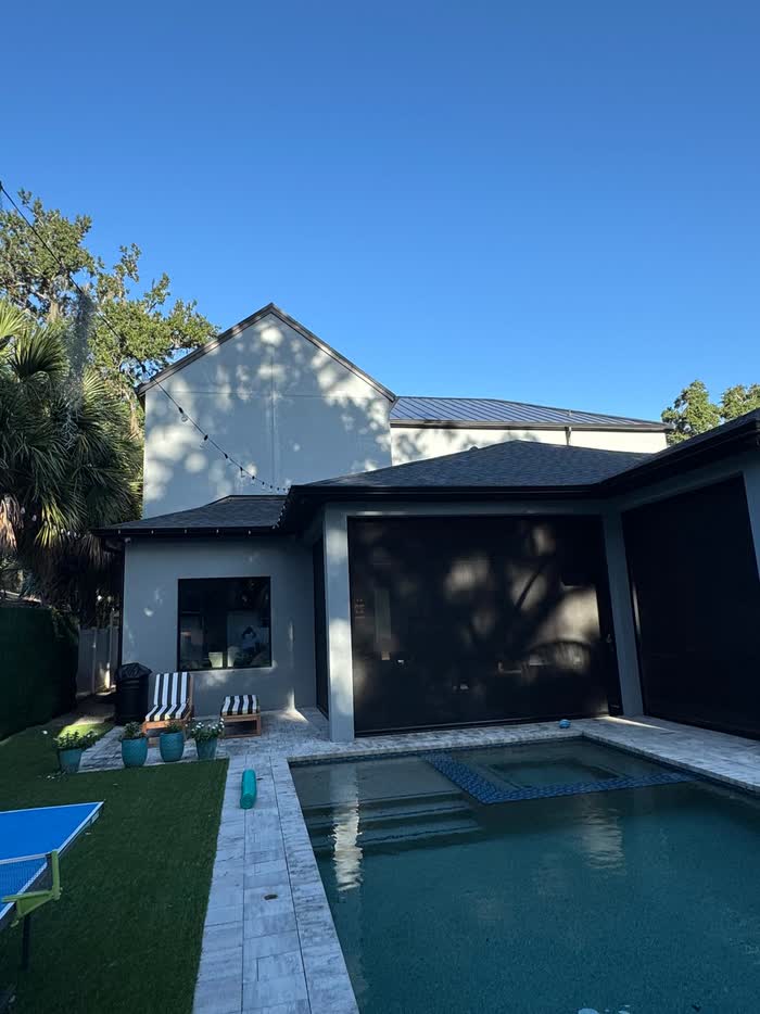 Tree shadows fall across the pale rear wall at dusk, with the dark screened porch beside the pool.