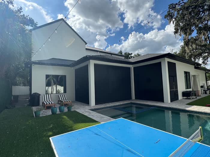 String lights run above the white rear wall and dark porch screens, a blue table tennis table poolside.