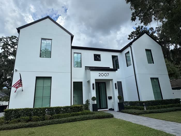 Front of a two-story white home with black-framed windows, a dark front door and a low hedge.