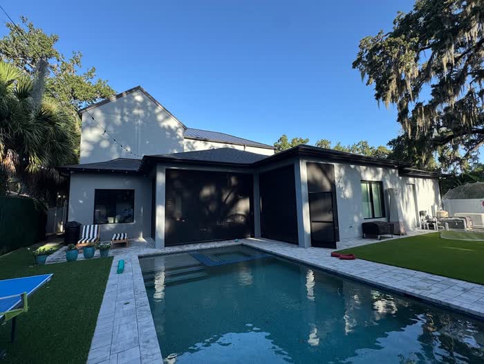 Low white house behind a long pool, a moss-draped oak overhanging the yard on a clear day.