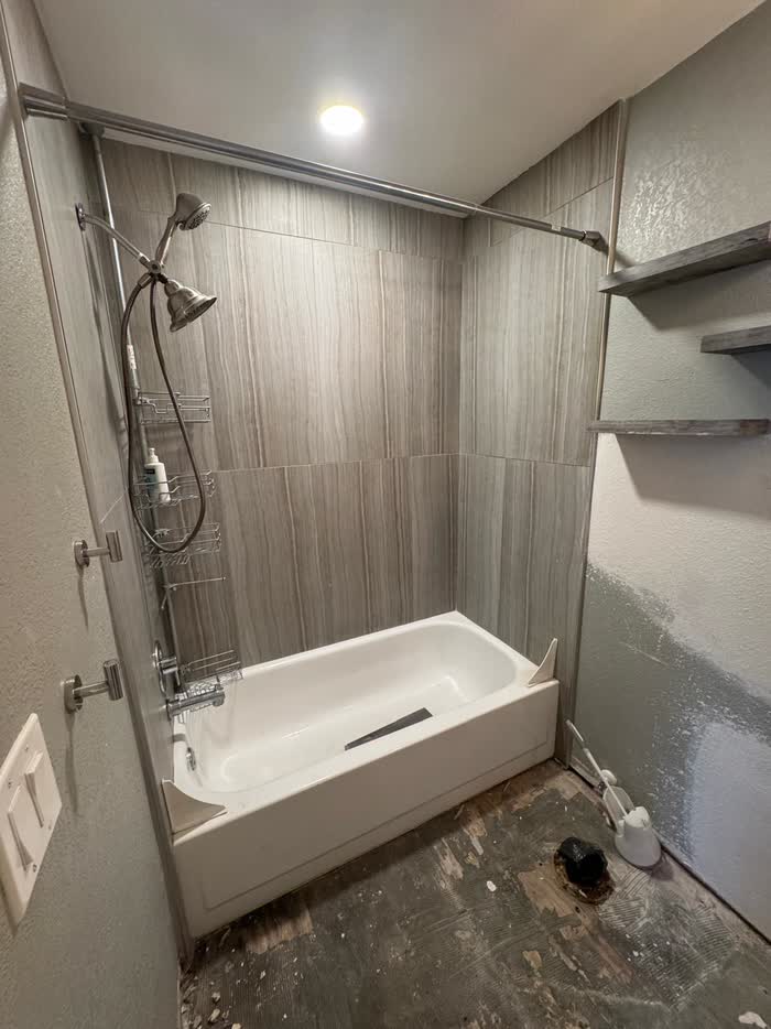 White tub set against grey veined wall panels, with a curved rod and handheld shower head.