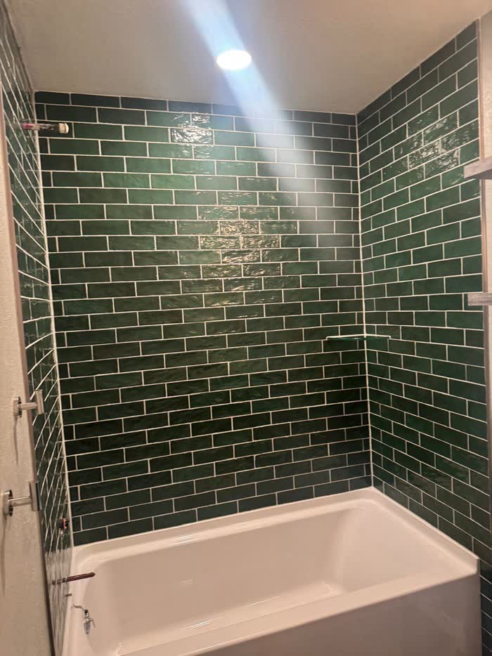 Deep green brick-shaped tiles cover a tub surround, lit by a single ceiling downlight.