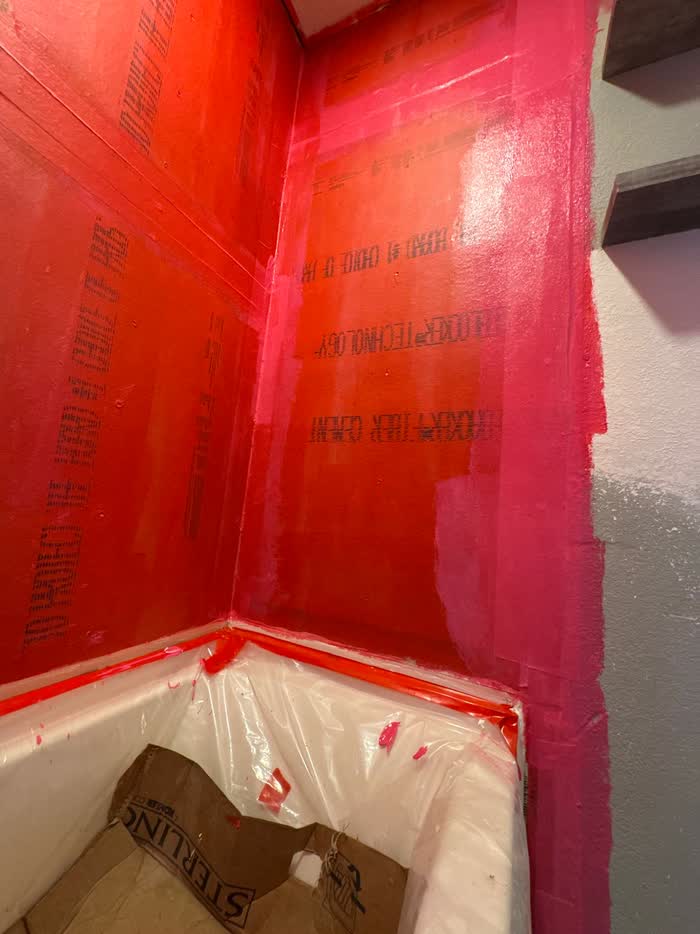 Bright pink and orange waterproof coating rolled onto shower walls above a tub masked with plastic.