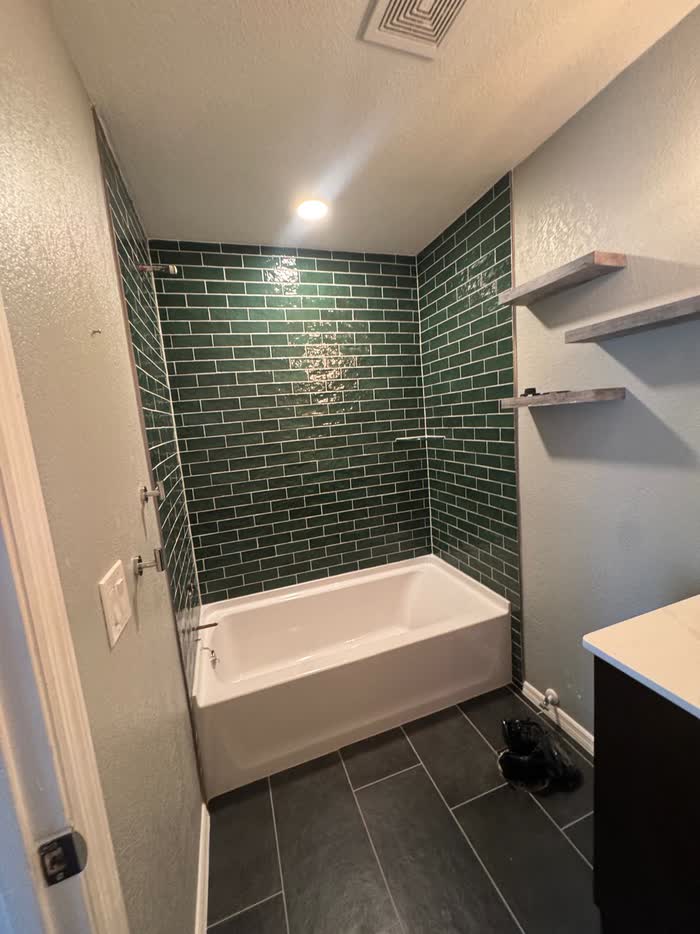 Finished bathroom with a green tiled tub surround, dark floor tiles and pale grey walls.
