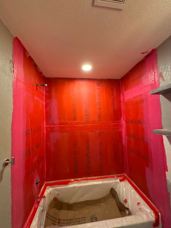 Shower alcove coated in vivid pink and orange, the tub protected under plastic sheeting and cardboard.