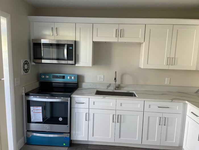New range and a deep sink set into a pale veined counter, white cabinets above and below.