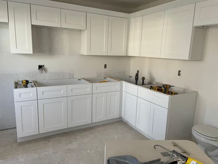 Drills and tools left on open cabinet bases in a kitchen still waiting on its counters.