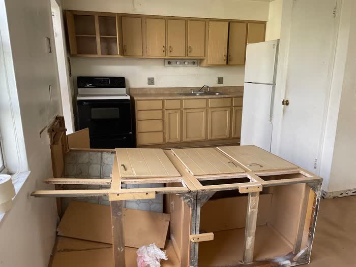 Cabinet doors laid across a torn-out peninsula frame in the middle of a kitchen demolition.