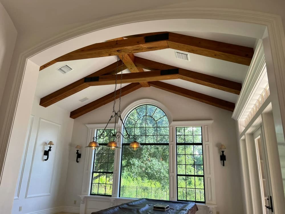 A vaulted ceiling with exposed beams over an arched window, wall lights either side.