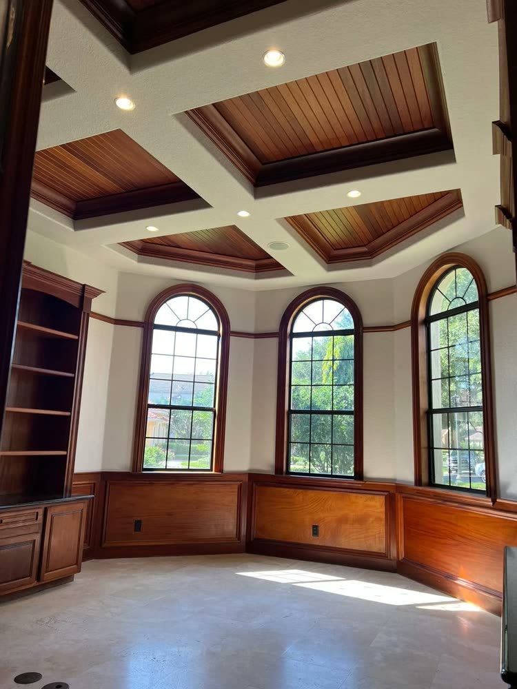 A study with a coffered ceiling in stained panels, three arched windows and panelled walls below.