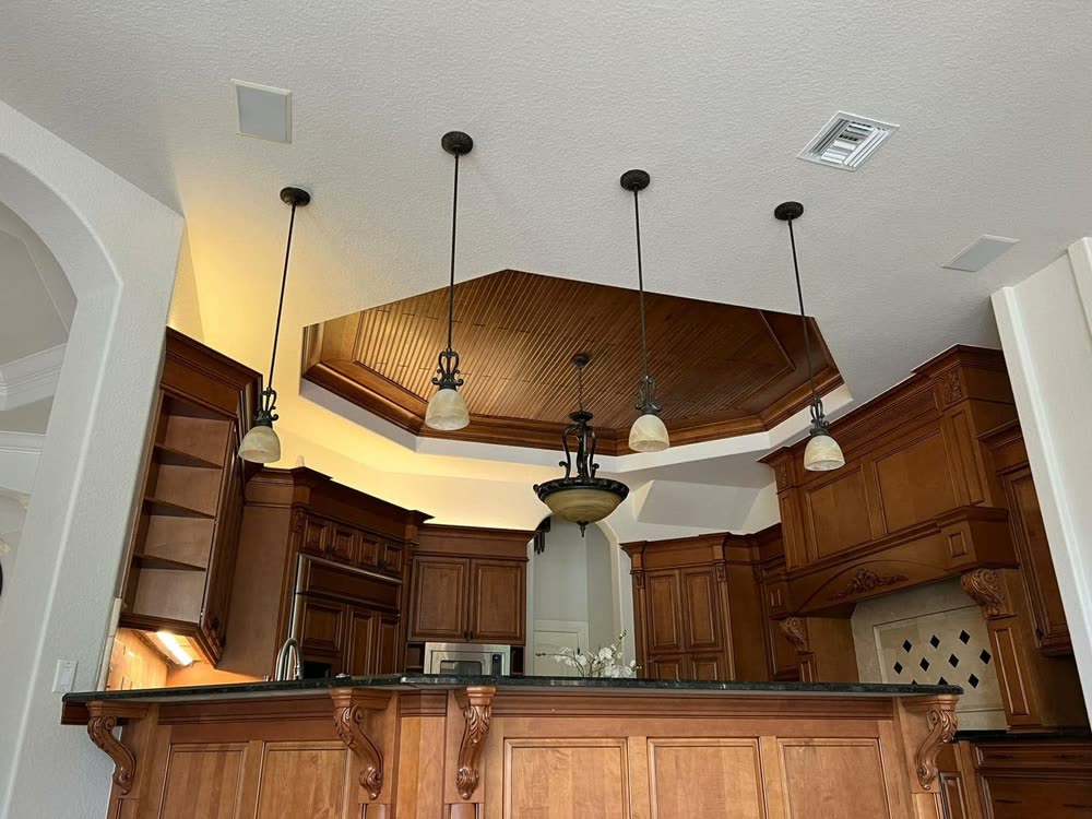 A kitchen with an octagonal recessed ceiling and pendant lights hanging over the counter.