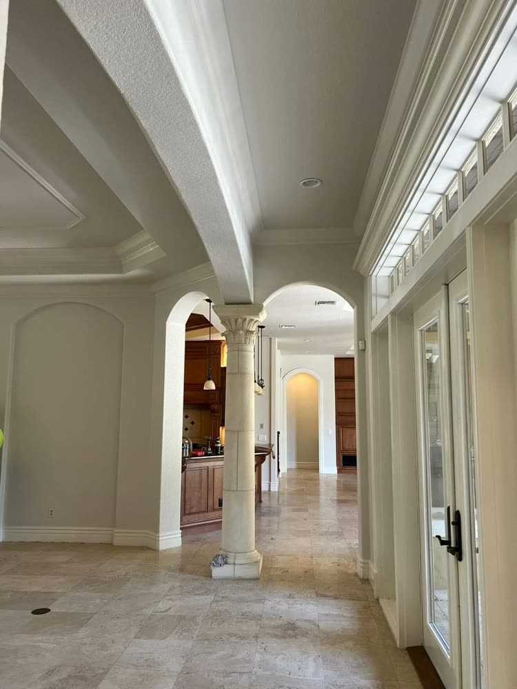 A hallway with a column and arched openings on one side and glazed doors along the other.