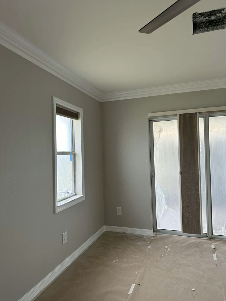A repainted room with crown moulding and a sliding door, the floor covered and taped.