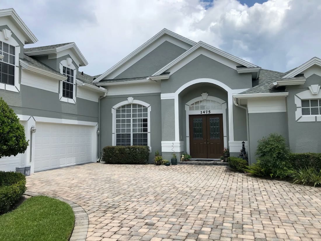 A repainted two-storey home in grey with white trim, an arched entry
              and a paver driveway.